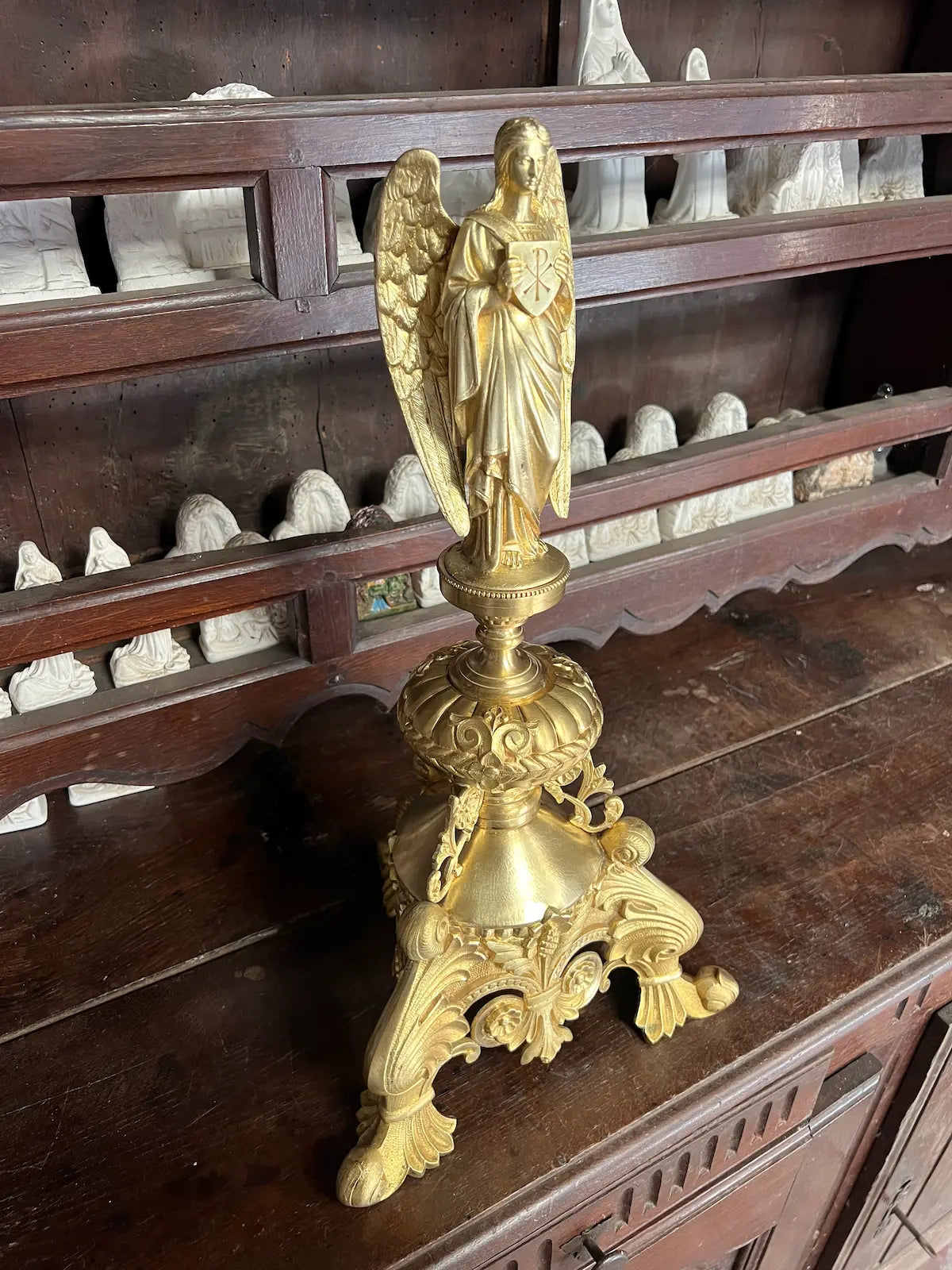 Antique gilded bronze angel holding a Christogram, ornate tripod base, 19th-century liturgical art.
/
Ange ancien en bronze doré tenant un Christogramme, base tripode ornementée, art liturgique du XIXe siècle.