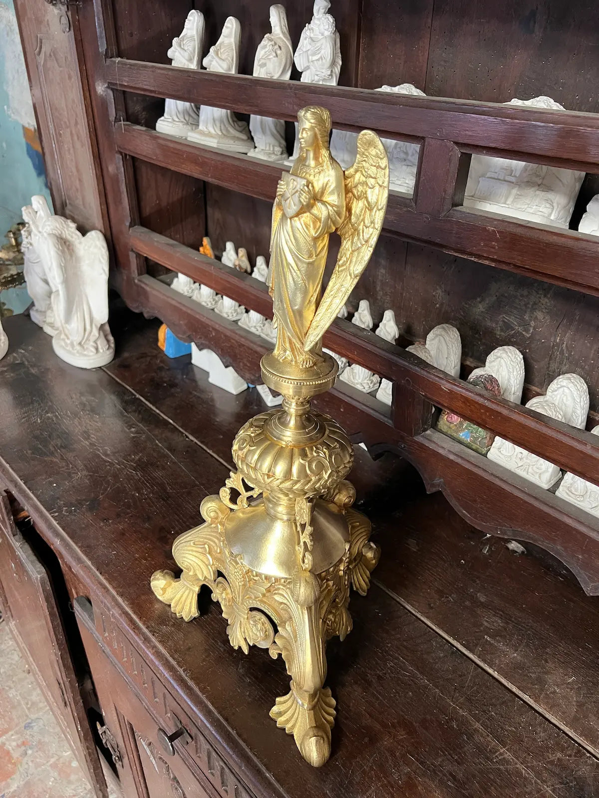 Antique gilded bronze angel holding a Christogram, ornate tripod base, 19th-century liturgical art.
/
Ange ancien en bronze doré tenant un Christogramme, base tripode ornementée, art liturgique du XIXe siècle.