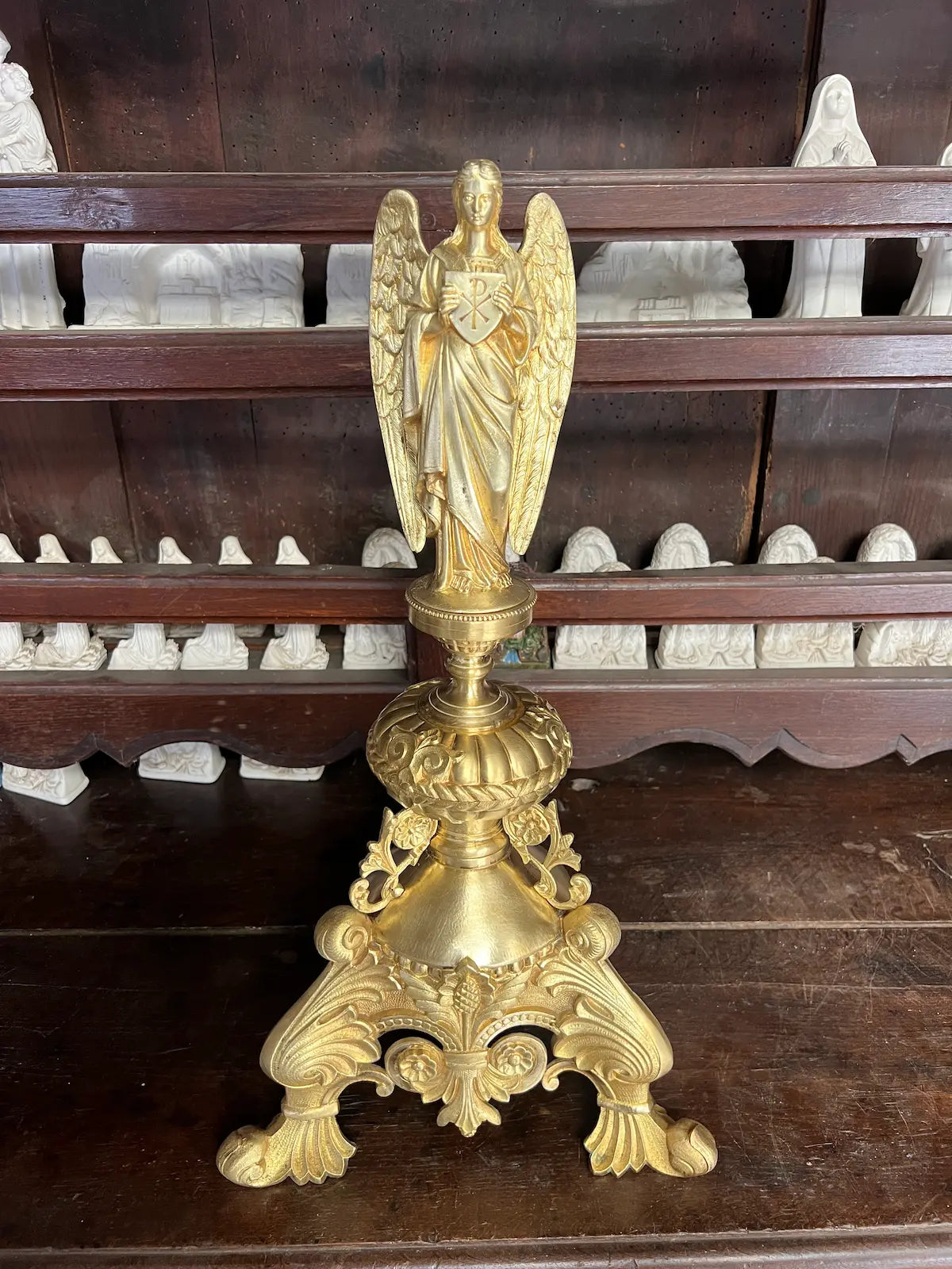 Antique gilded bronze angel holding a Christogram, ornate tripod base, 19th-century liturgical art.
/
Ange ancien en bronze doré tenant un Christogramme, base tripode ornementée, art liturgique du XIXe siècle.