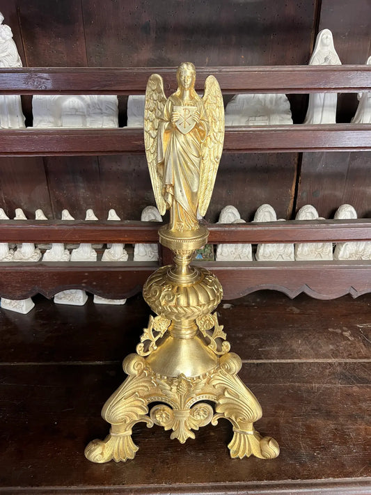 Antique gilded bronze angel holding a Christogram, ornate tripod base, 19th-century liturgical art.
/
Ange ancien en bronze doré tenant un Christogramme, base tripode ornementée, art liturgique du XIXe siècle.