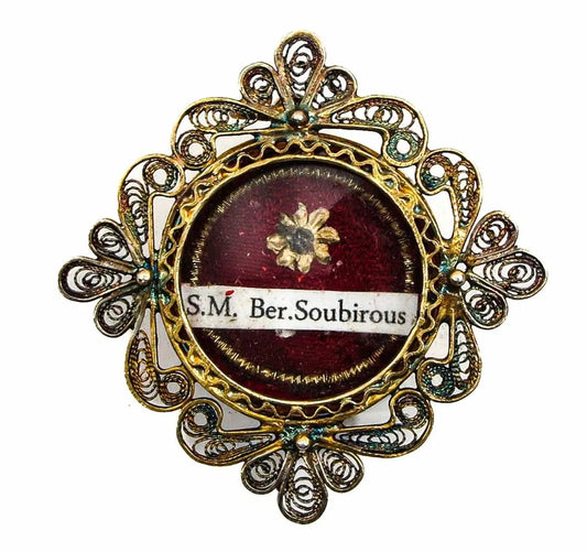 Antique reliquary of Saint Bernadette Soubirous with gilt filigree frame and relic on red background
/
Reliquaire ancien de Sainte Bernadette Soubirous avec monture filigranée dorée et relique sur fond rouge